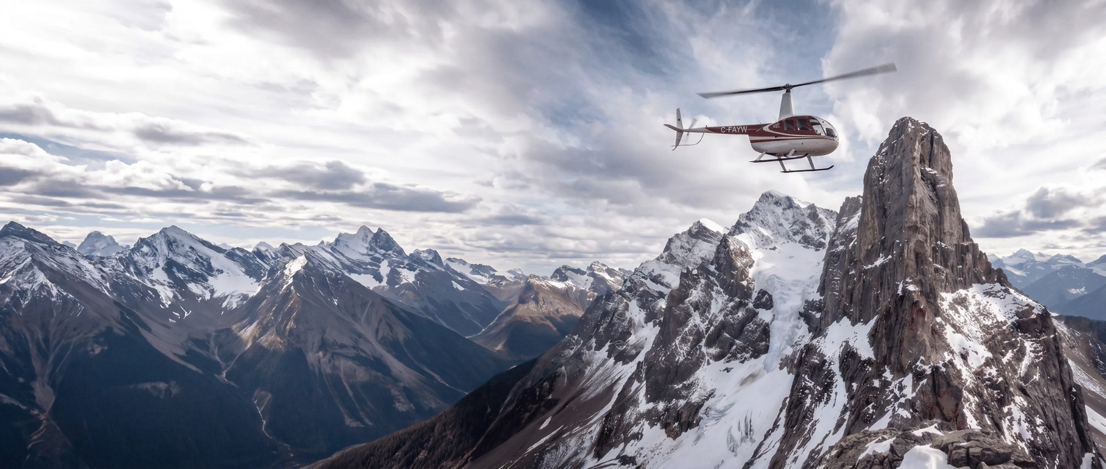 Robinson R44 flying beside a snow-capped peak in the Canadian Rockies